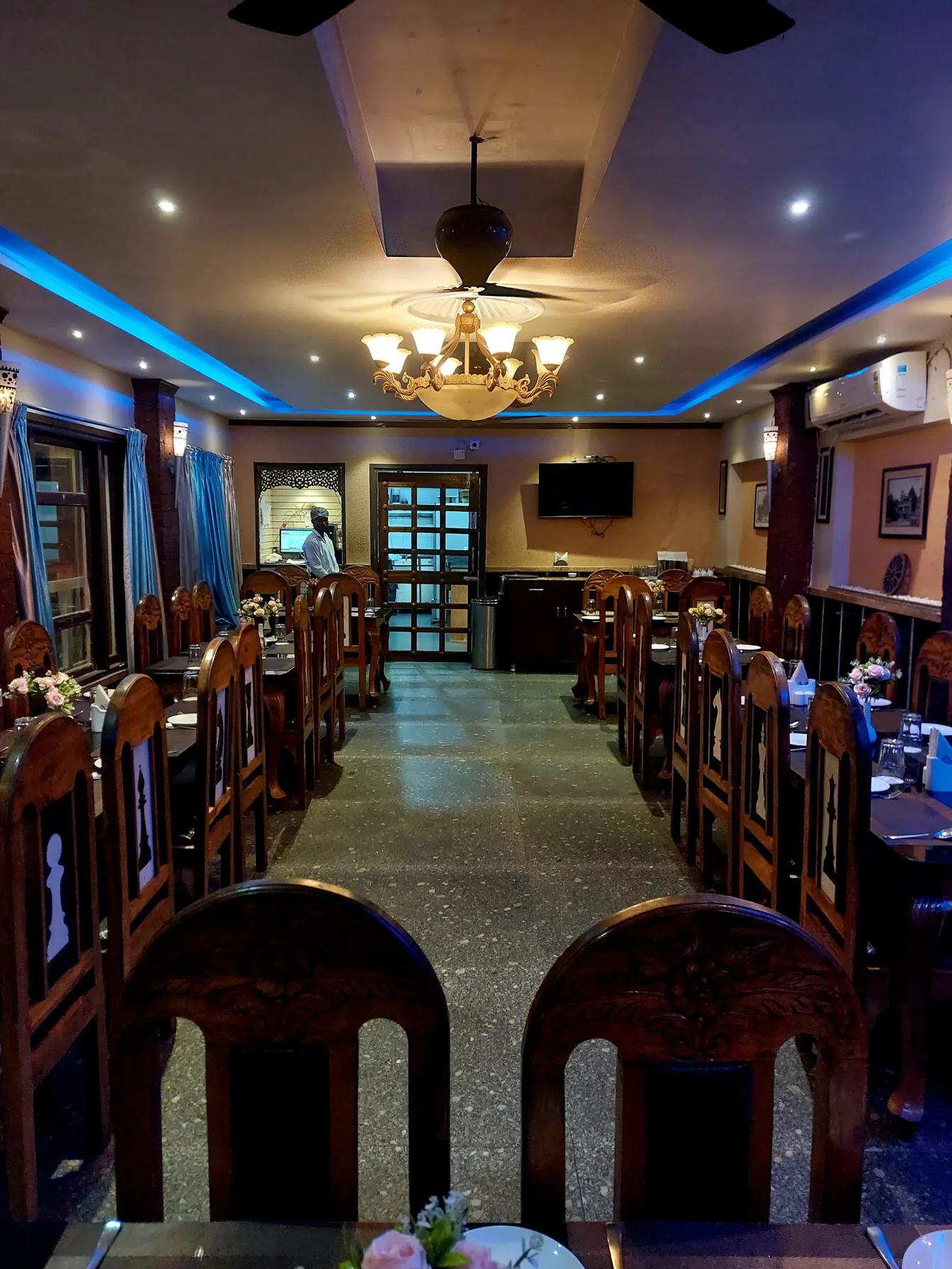 Byanjan dining hall in the evening, carved chairs along the aisle under a chandelier