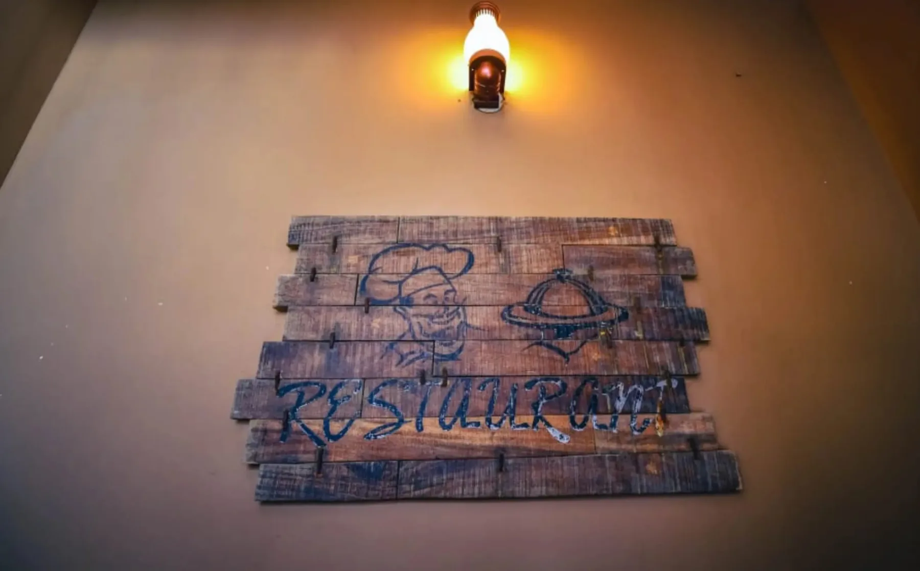 Hand-painted wooden restaurant sign at Byanjan, lit by a warm wall lamp