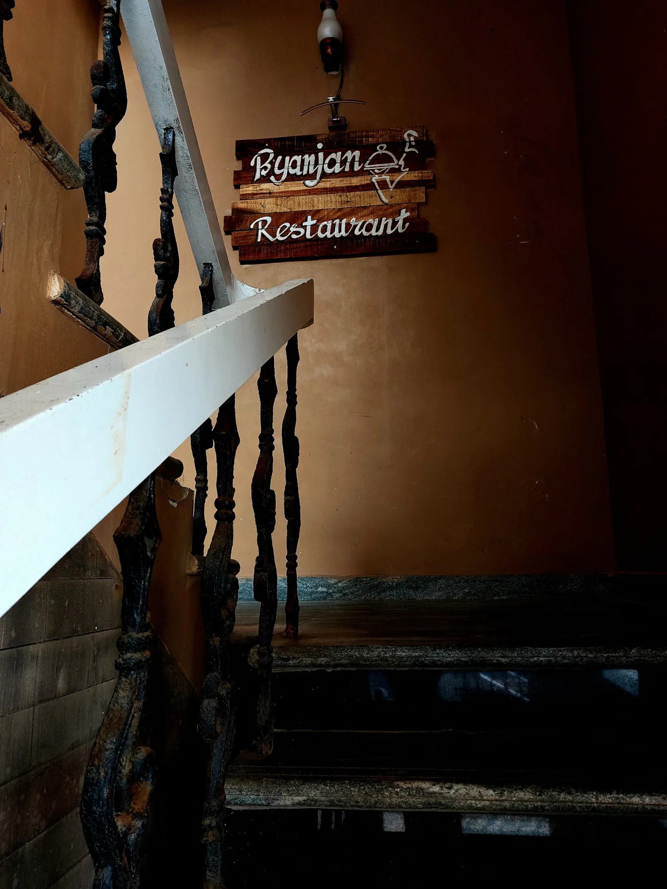 The Byanjan restaurant sign on the wall beside the stair, under a wall lamp